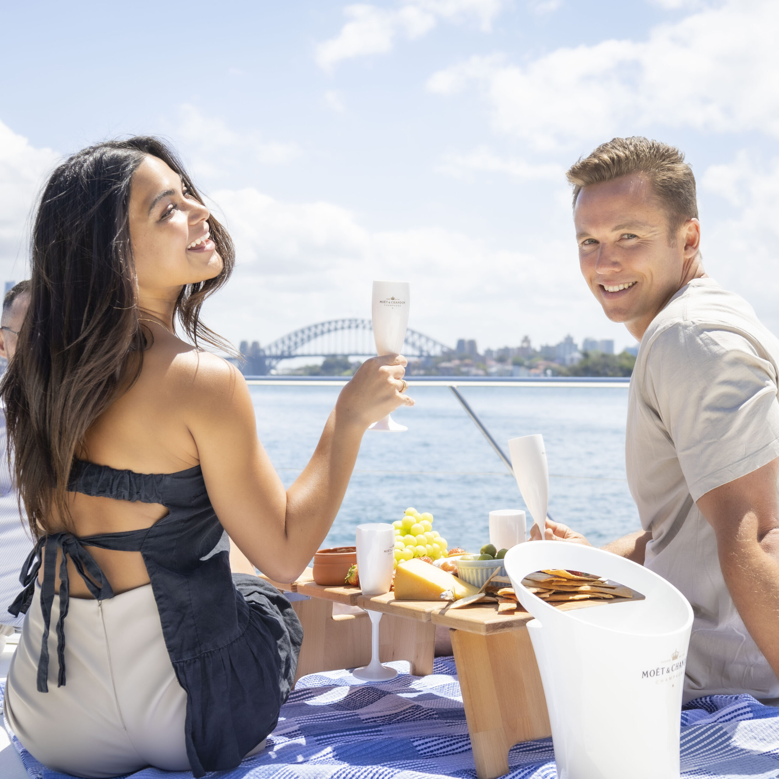 Guests toasting champagne over a grazing platter aboard MV Yarranabbe with the Sydney Harbour Bridge behind